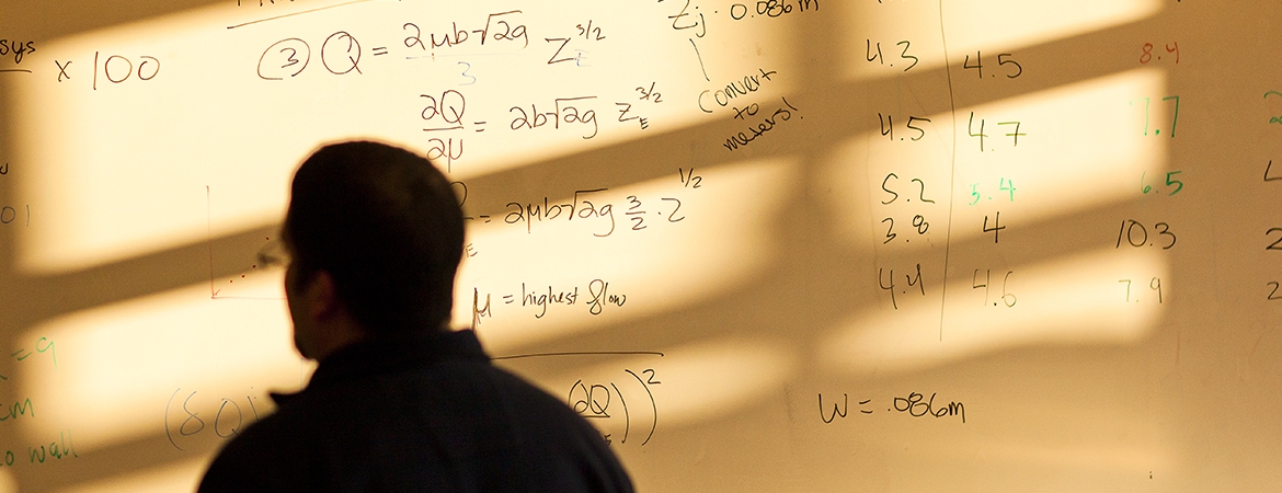 silhouette of a student in front of a whiteboard with equations written on it